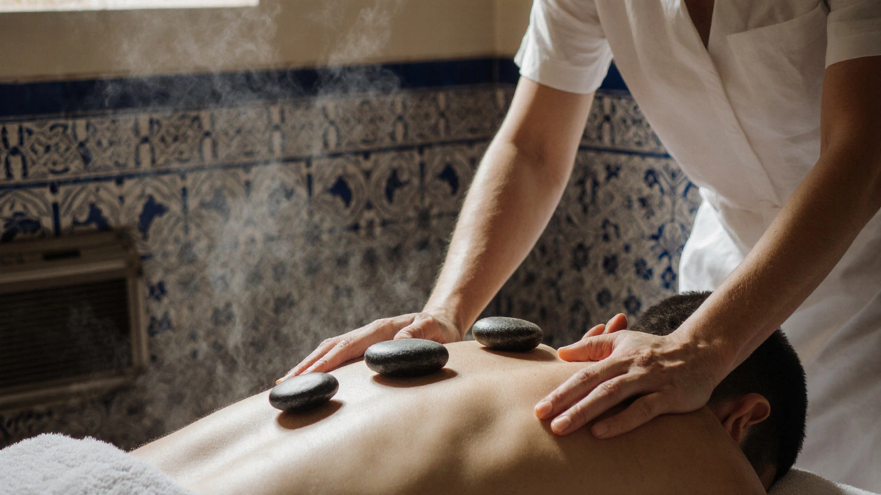 A therapist using warm stones along a client&#039;s back in a tiled Hammam room, steam rising softly.